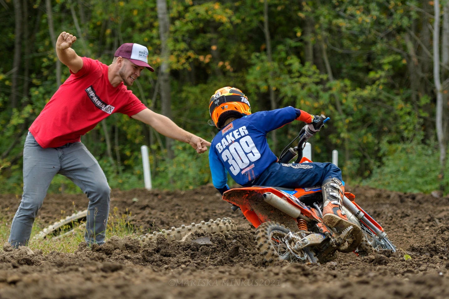 Man cheers on child riding dirt bike on muddy track.