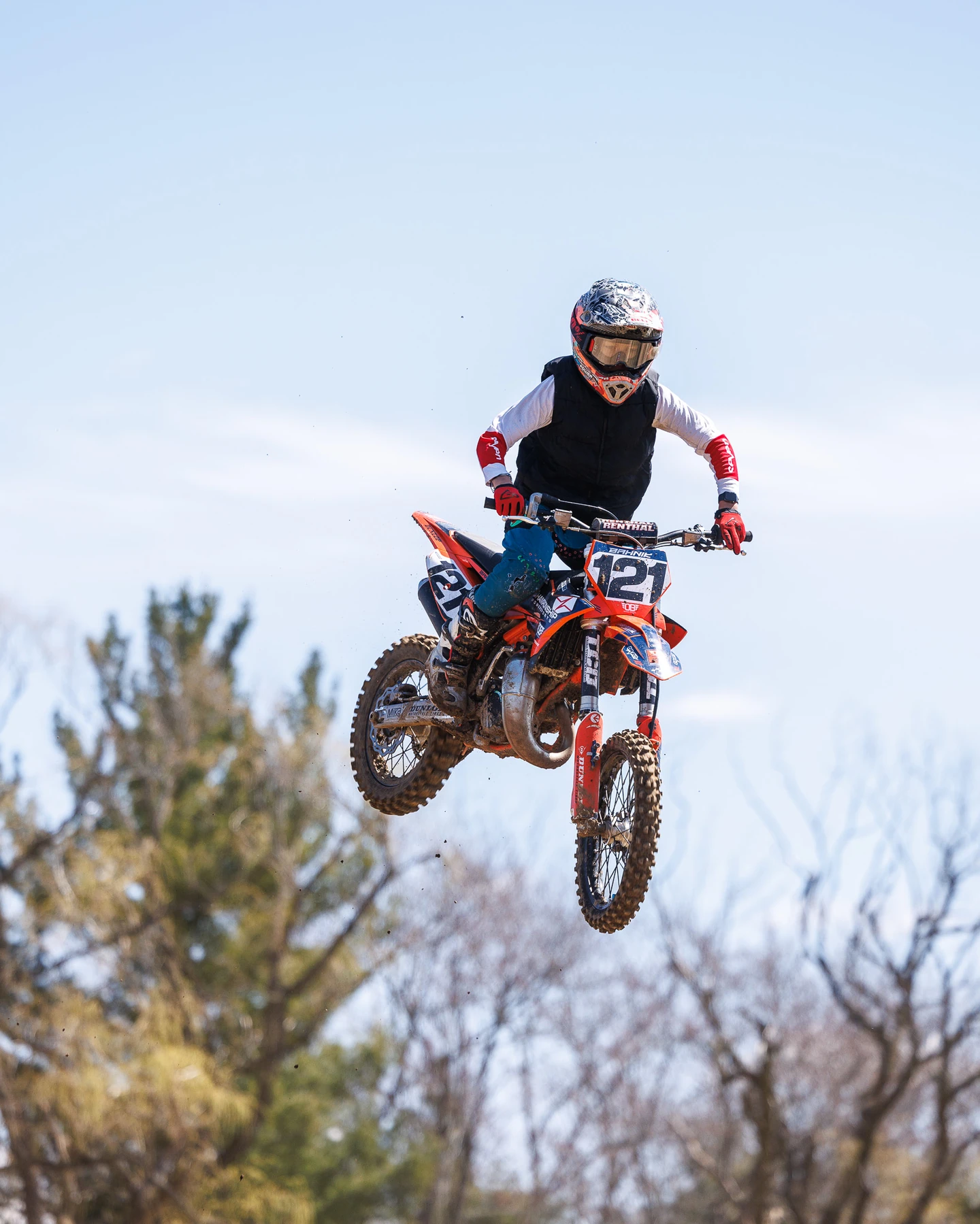 Motocross rider mid-air on orange dirt bike, number 121.