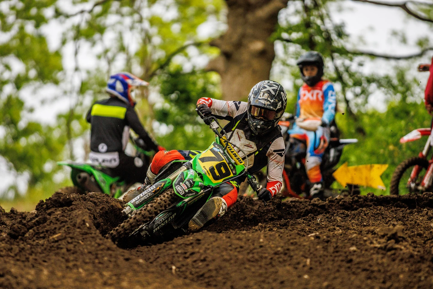Motocross rider on green bike cornering on dirt track.