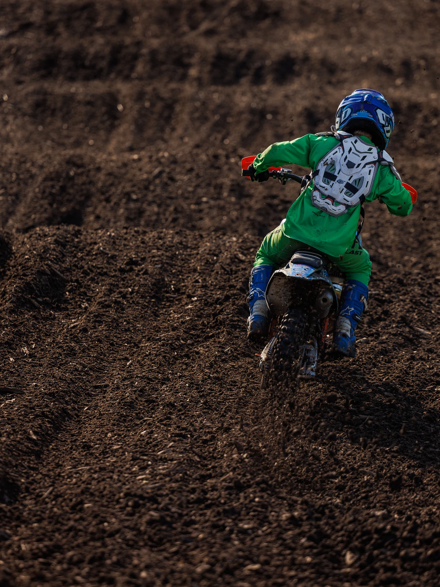 Young dirt biker in green on a dirt track.