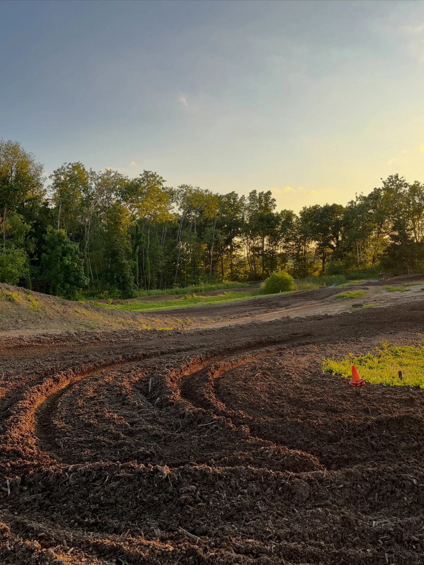 Dirt bike track at sunset with tire tracks and trees.