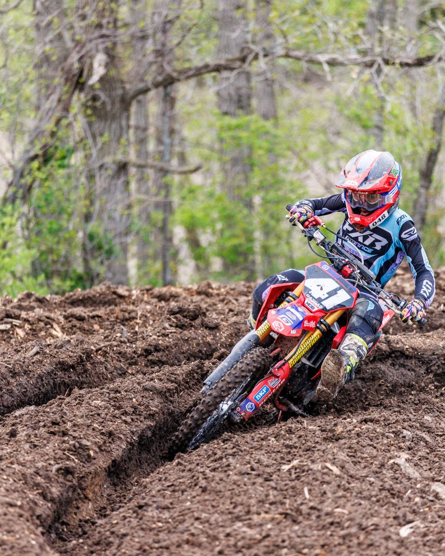 Motocross rider on red dirt bike navigating muddy track turn.
