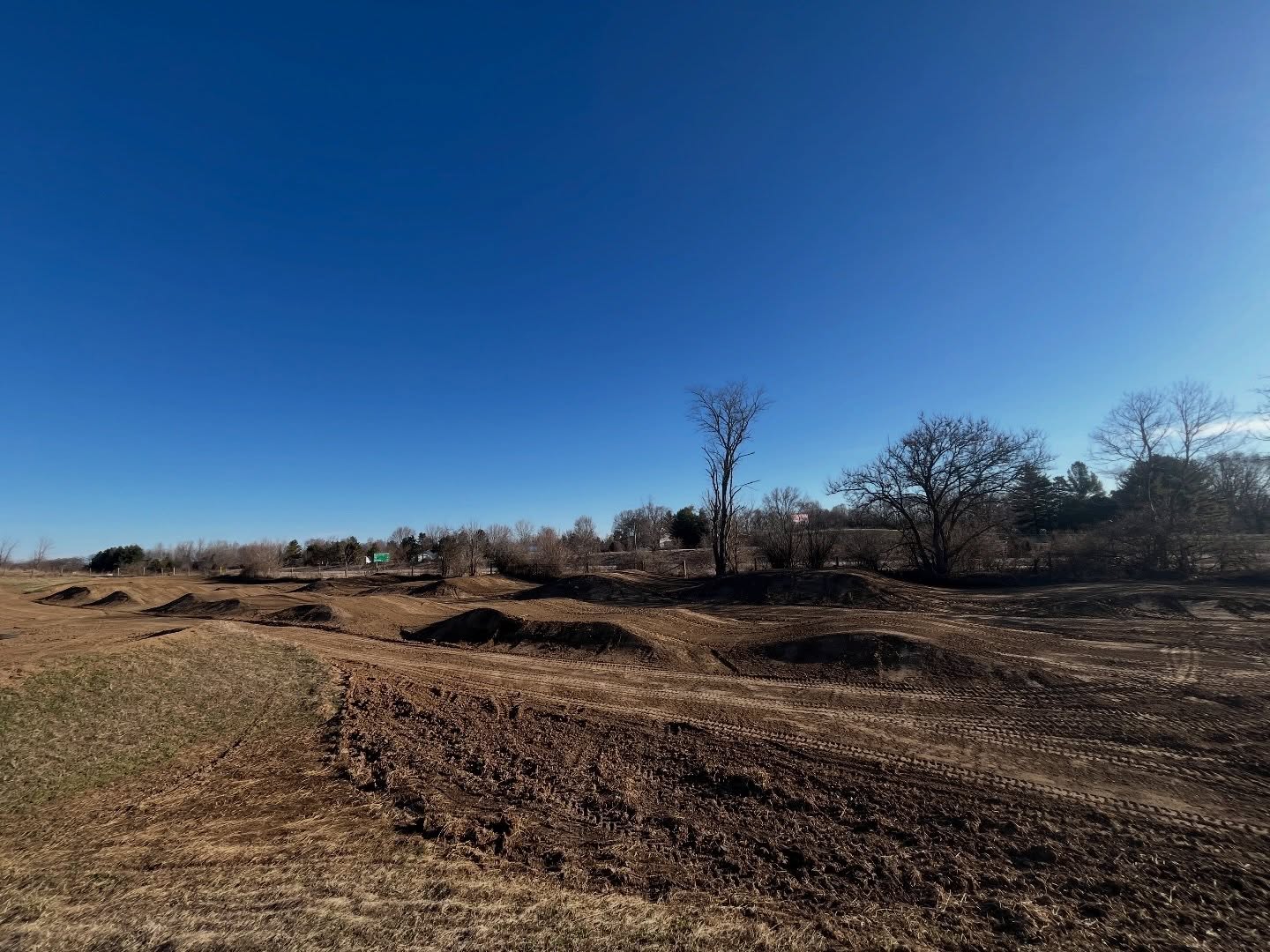 Empty dirt motocross track with jumps under clear blue sky.